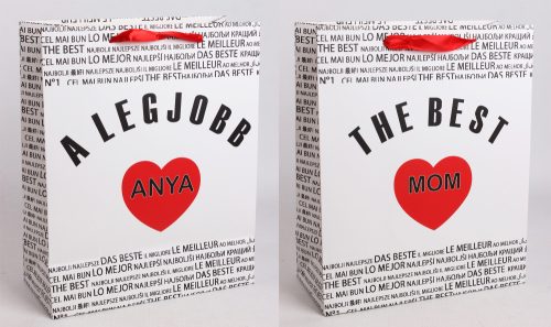 PAPÍRTASAK MATT, SZALAG FÜLLEL, FEHÉR ALAPON FEKETE NEMZETKÖZI ÍRÁSSAL A HÁTTÉRBEN, A LEGJOBB ANYA/ THE BEST MOM FELIRATTAL, PIROS SZÍVVEL